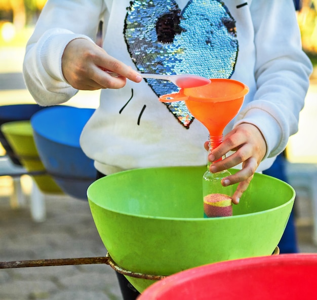 Il bambino versa la sabbia colorata nella bottiglia. Attività diurne nel parco.