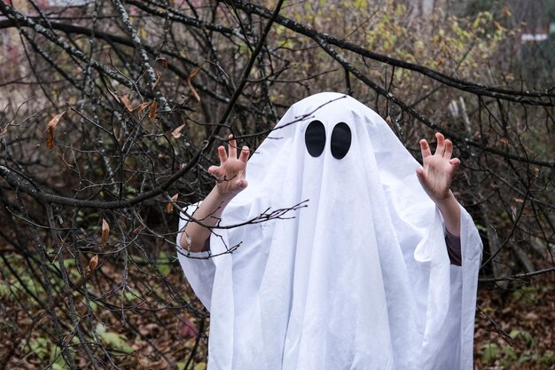 Il bambino vestito con un costume da fantasma spaventa nella foresta oscura Il bambino si diverte ad Halloween