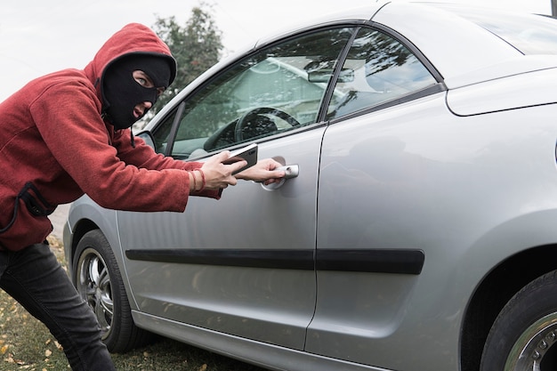 Il bandito mascherato apre la serratura centrale di un'auto moderna e costosa con l'aiuto di un telefono cellulare. Connettiti a MirrorLink.