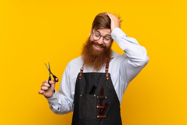 Il barbiere con la barba lunga in un grembiule su sfondo giallo isolato ha realizzato qualcosa e intendendo la soluzione