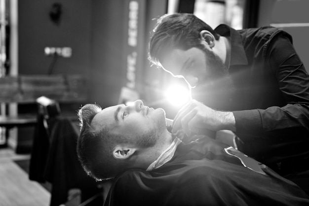 Il barbiere in procinto di tagliare la barba di un cliente in un barbiere, foto in bianco e nero