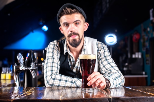 Il barista barbuto crea un cocktail stando in piedi vicino al bancone del bar