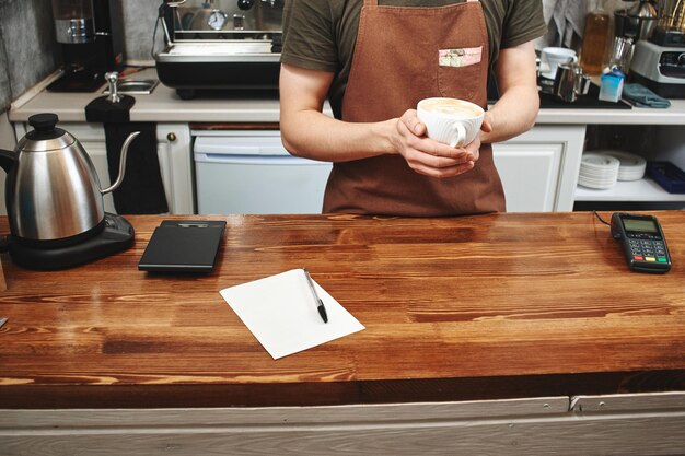 Il barista è in piedi dietro il bancone della caffetteria con in mano una tazza