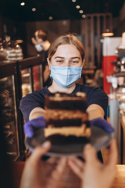 Il barista è vestito con una maschera medica e guanti passa l'ordine al cliente nel bar