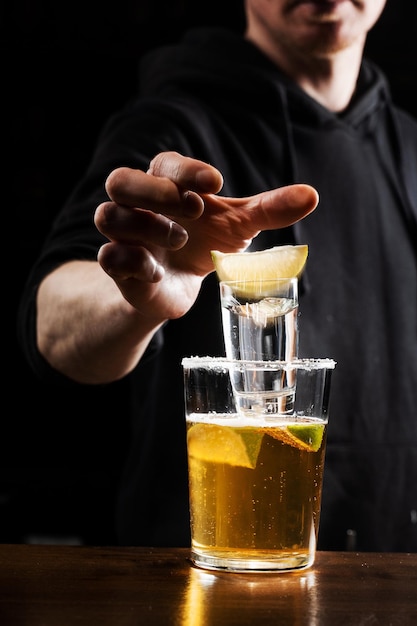 Il barista fa cadere un colpo di tequila con calce nel bicchiere di birra Cocktail alcolico Morte del messicano su sfondo nero