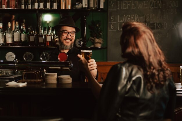 Il barista felice serve birra alla spina in vetro al bar a una donna