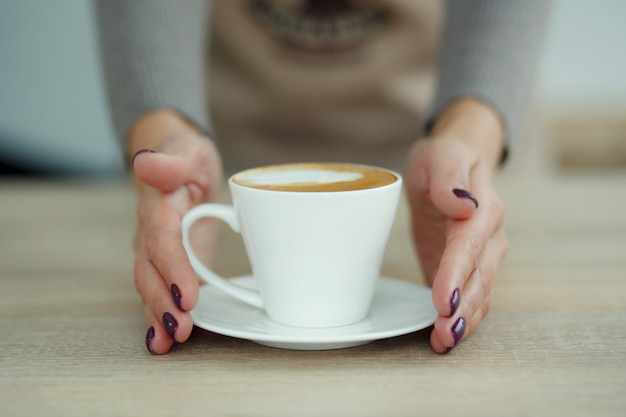 Il barista in grembiule nella caffetteria dà appena preparato il caffè fresco al cliente