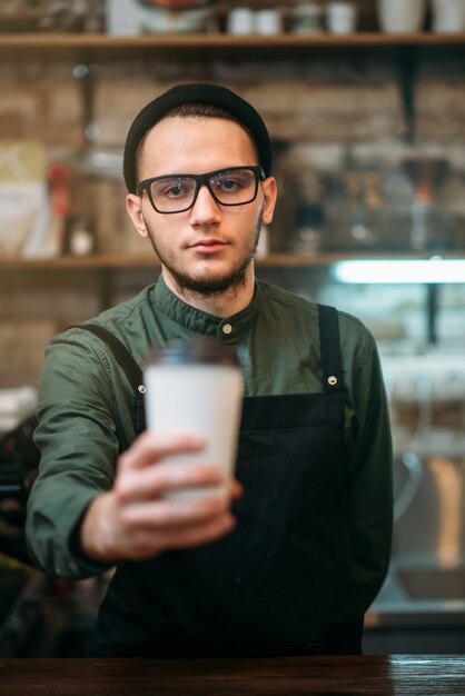 Il barista in grembiule nero allunga il bicchiere di plastica