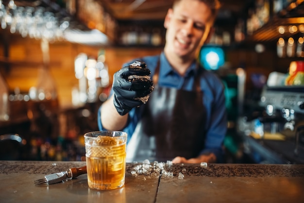 Il barista maschio lavora con il ghiaccio al bancone del bar