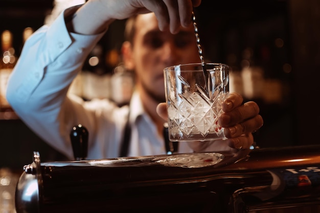 Il barista prepara un cocktail con ghiaccio in un bicchiere al bar