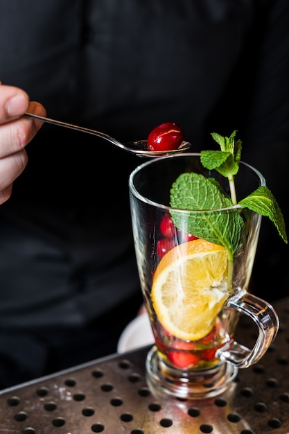 Il barista prepara un tè alla frutta con mirtilli rossi in un bicchiere