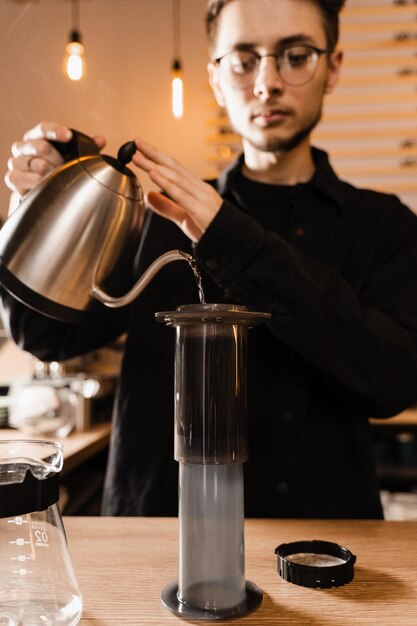 Il barista sta versando acqua calda dal bollitore all'aeropress Processo di preparazione dell'aeropress Versare acqua calda sui chicchi di caffè tostati e macinati nell'aeropress