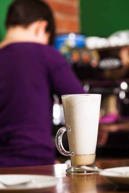 Il barista sta versando il latte in un bicchiere con caramello - preparando un caffè latte dolce e speziato