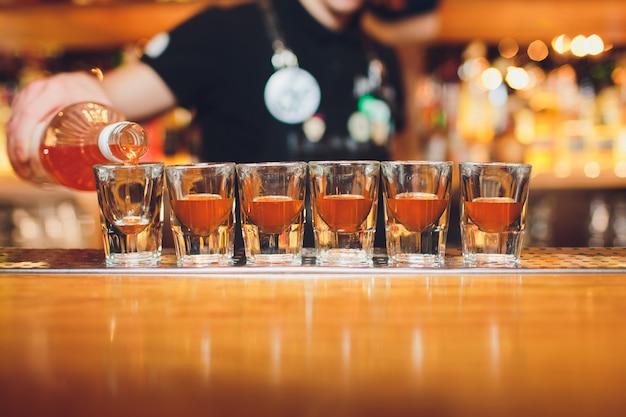 Il barista versando una forte bevanda alcolica in piccoli bicchieri sul bar, colpi.