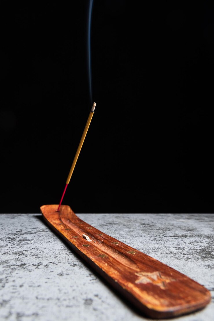 Il bastoncino di incenso che brucia si trova su un supporto di legno su sfondo nero