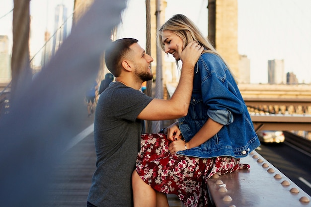 Il bei giovane uomo e donna posano sul ponte di Brooklyn nei raggi del sole del mattino