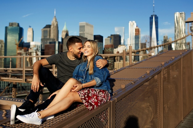 Il bei giovane uomo e donna posano sul ponte di Brooklyn nei raggi del sole del mattino