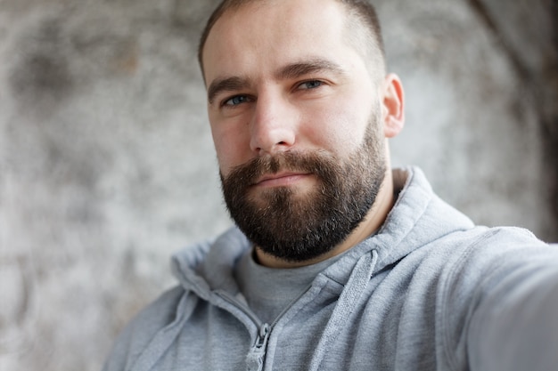 Il bel giovane con la barba in camicia a scacchi si fa da solo, sorridente, su uno sfondo grigio gray