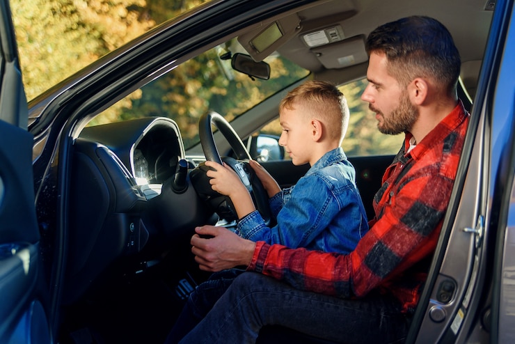 Il bel padre che indica qualcosa mentre insegna al figlio adolescente a guidare l'auto