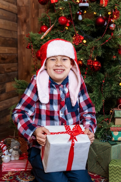 Il bel ragazzino accanto all'albero di Natale è felice con un regalo