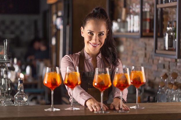 Il bellissimo barista serve cinque cocktail all'arancia in bicchieri di vino in un bar.