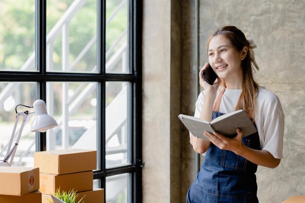 Il bellissimo imprenditore asiatico apre un negozio online È al telefono con un cliente per confermare l'ordine che invia merci tramite un concetto di società di corriere di una donna che apre un'attività online