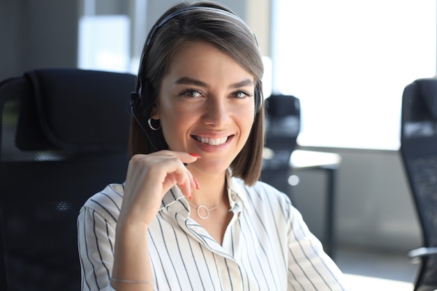 Il bellissimo lavoratore di call center sorridente in cuffia sta lavorando in un ufficio moderno.