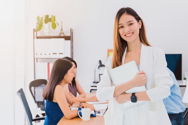 Il bello asiatico autorizza il computer portatile e l'amico della tenuta della donna che lavorano alla sala riunioni in ufficio. Proprietario imprenditrice avvio con fiducioso e allegro.