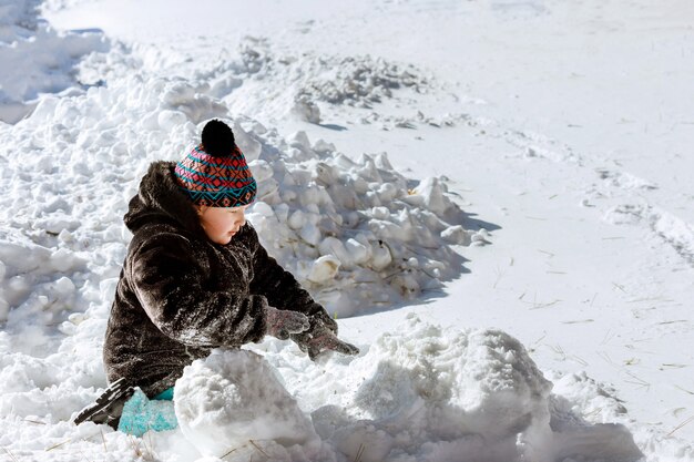 Il bello bambino felice gioca con neve in un'iarda del paese