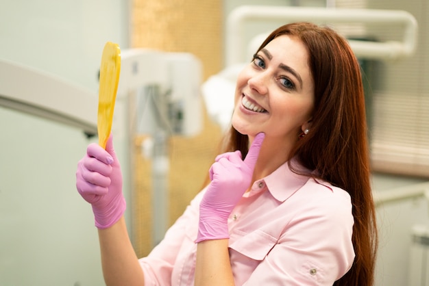 Il bello dentista femminile mostra i denti sani. Sorridere e tenere uno specchio. Odontoiatria e igiene orale.