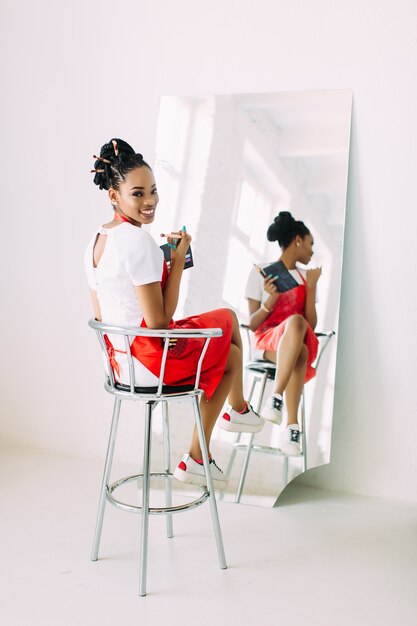 Il bello giovane insieme afroamericano della tenuta della donna dell'estetista di compone le spazzole e la sorveglianza nello specchio