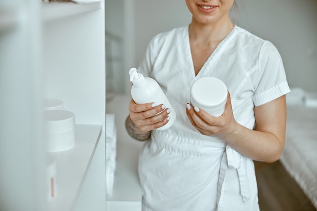 Il bello massaggiatore femminile caucasico felice sta posando nel salone di trattamento moderno minimalista bianco