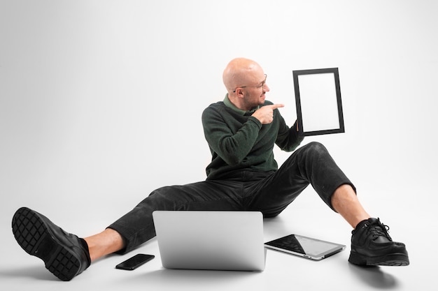 Il bello uomo tiene un telefono, un tablet e un computer portatile, comunica e funziona.