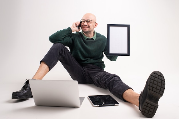 Il bello uomo tiene un telefono, un tablet e un computer portatile, comunica e funziona.