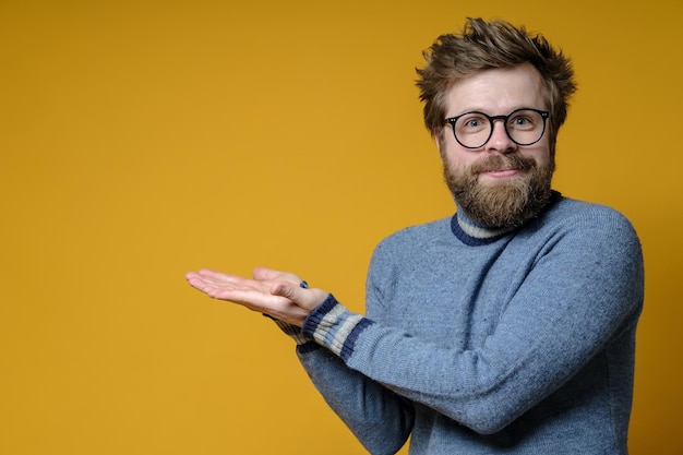 Il benevolo uomo irsuto in un maglione lavorato a maglia fa un gesto con le mani che puntano a qualcosa