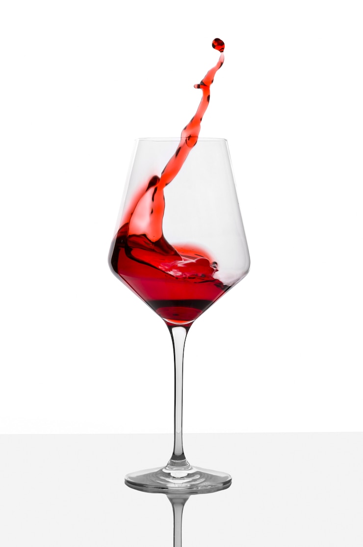 Foto il bicchiere di vino rosso con spruzza sulla tavola bianca.