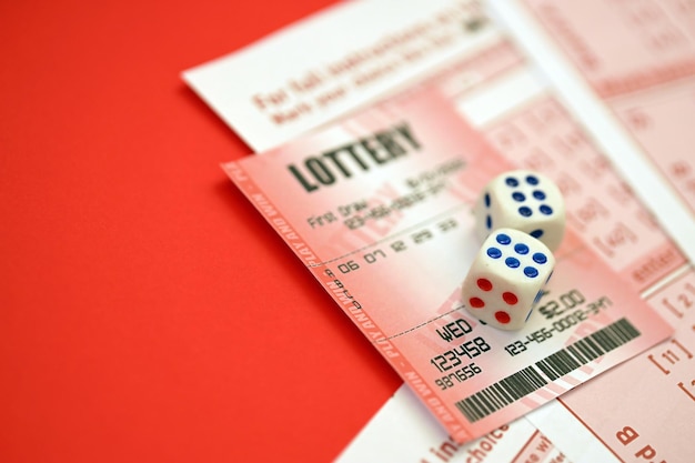 Il biglietto della lotteria rosso con dadi giace su fogli di gioco rosa con numeri per la marcatura per giocare alla lotteria Concetto di gioco della lotteria o dipendenza dal gioco Primo piano