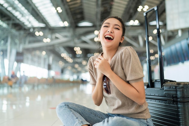 Il blocco è finito nel tempo per viaggiarefelicità viaggiatore femminile asiatico indossare panno casual gesto dell'onda della mano sorridente mentre si siede rilassarsi sul pavimento dell'aeroporto del terminal con il concetto di viaggio di sicurezza dei bagagli