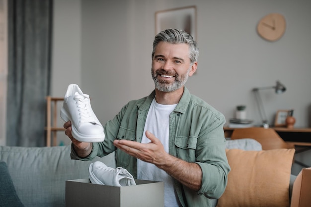 Il blogger europeo senior felice sorridente con la barba registra la recensione video sulle scarpe disimballa la scatola con gli acquisti