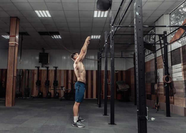 Il bodybuilder maschio atletico si esercita con la palla medica in palestra. Allenamento funzionale