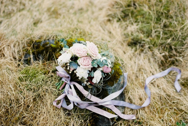 Il bouquet da sposa si trova su una pietra ricoperta di muschio tra l'erba secca