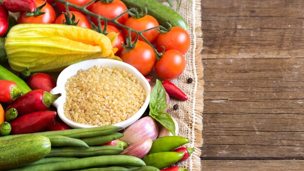 Il bulgur organico crudo in una ciotola con le verdure si chiude su su una tavola di legno con lo spazio della copia