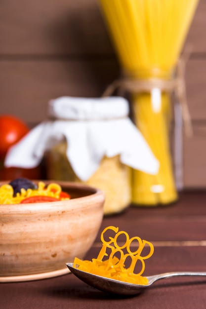 Il buon cibo è allineato con la pasta su un cucchiaio vicino a un piatto con pasta pronta