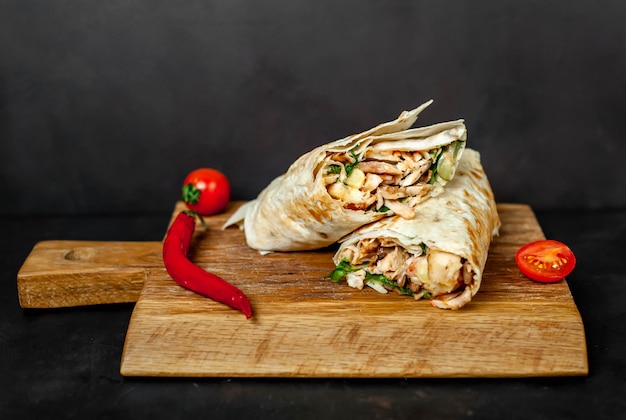 Il burrito si avvolge con pollo e verdure su un tagliere, su uno sfondo di cemento, shawarma messicano