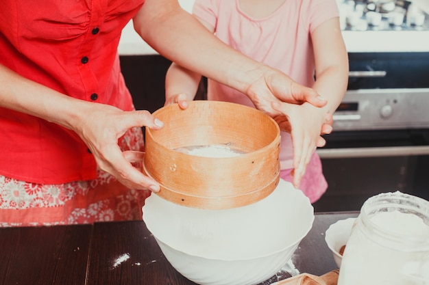 Il busto di mamma e figlia in piedi in cucina e filtrare la farina attraverso il setaccio