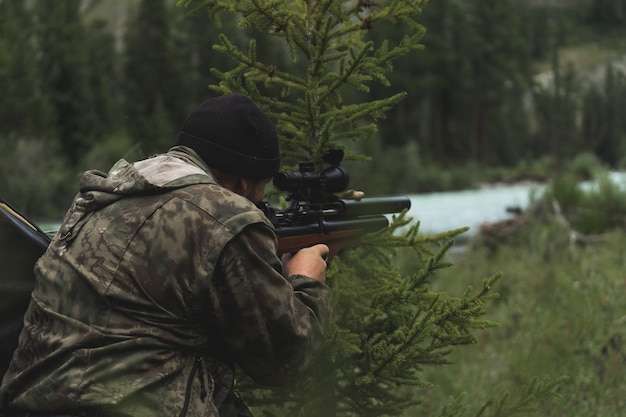 Il cacciatore mira con un fucile. Un uomo in mimetica si prepara a sparare. A caccia nel bosco con un fucile da cecchino