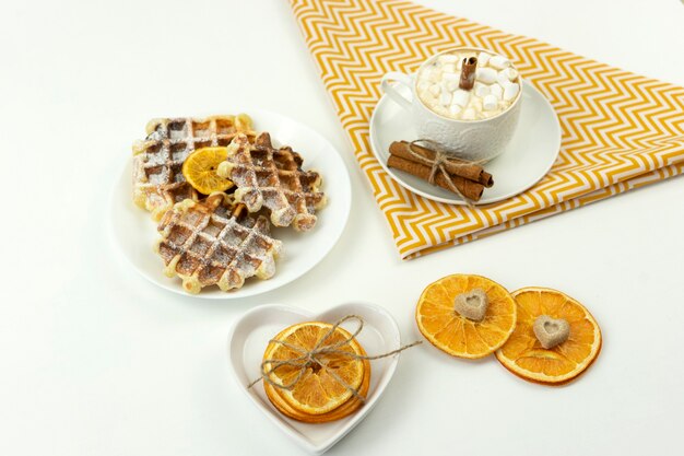 Il caffè della prima colazione con marshmallow e un bastoncino di cannella e waffle belgi giace su un tavolo