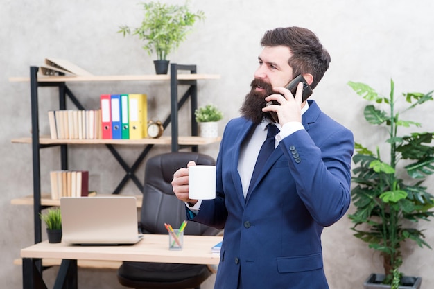 Il caffè è garanzia di negoziazioni di successo Dipendente dalla caffeina Uomo d'affari barbuto tenere tazza e smartphone Chiamata mobile Inizia la giornata con il caffè Pausa rilassante caffè Capo che si gode una bevanda energetica