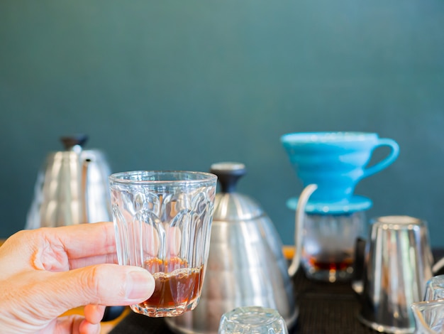 Il caffè nero caldo viene estratto dal processo di gocciolamento in un caffè espresso tenuto in mano da un uomo.