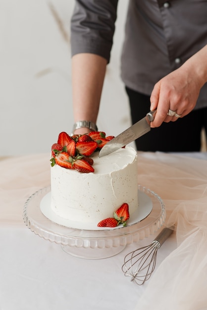 Il cameriere della donna taglia con una torta alla crema bianca del coltello con le fragole sul tavolo